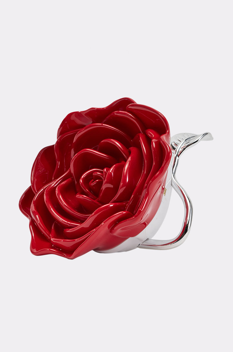 A glossy, rose-shaped red ceramic teacup with a silver handle and leaf detail, echoing the design of the ROSE PETAL PURSE, set against a plain white background.