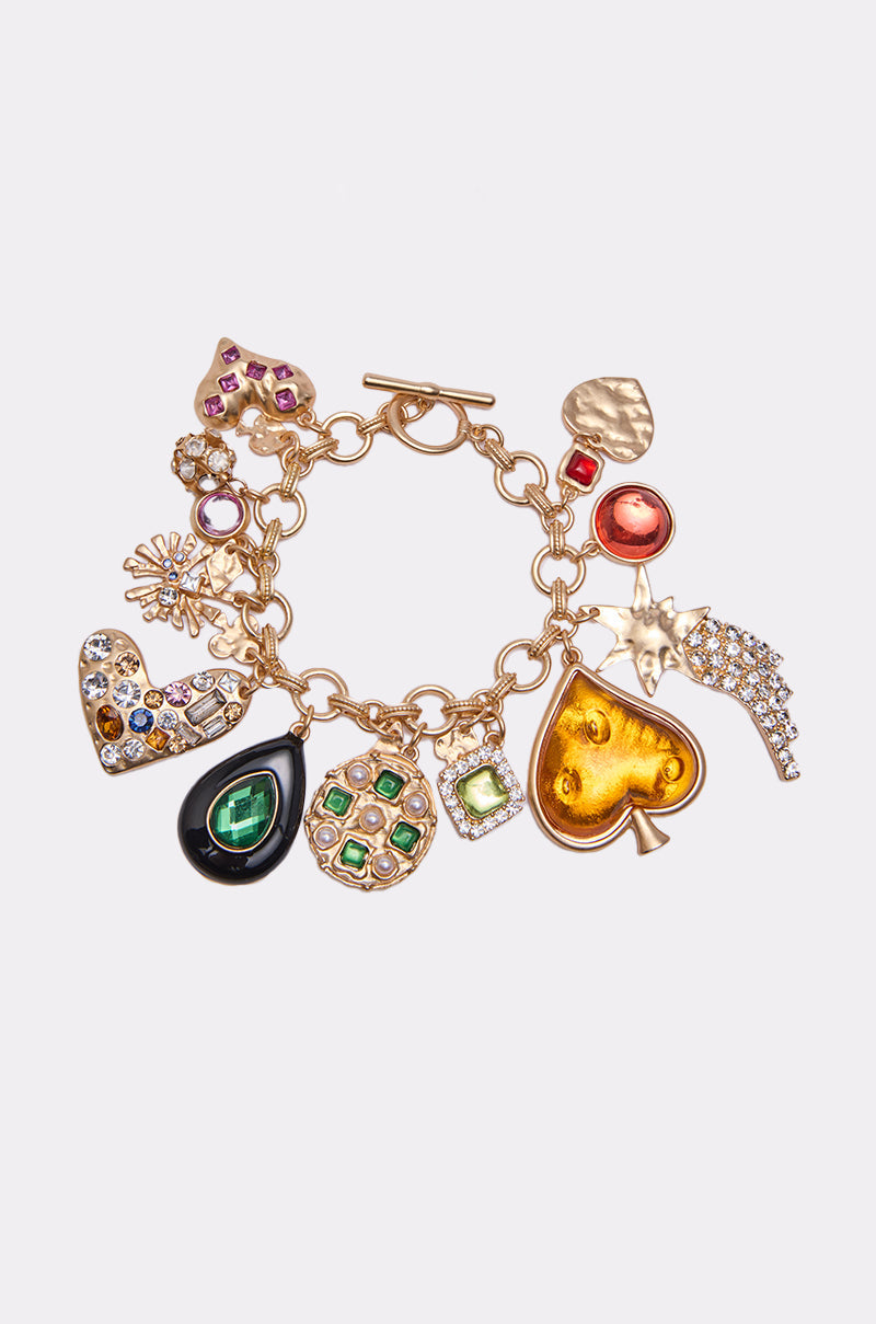 The IN EUROPE CHARM BRACELET is a gold-tone chain adorned with colorful jewels—hearts, a green teardrop, yellow spade, starburst, and ornate charms—beautifully displayed on a plain white background. 0