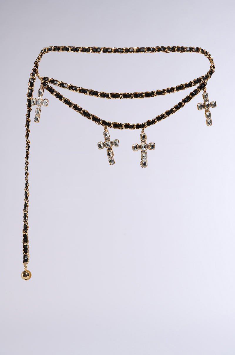 The CROSS MY HEART CHAIN BELT is a gold chain belt with an adjustable fit and black accents, featuring four crystal-adorned cross charms. It has a tiered design with a dangling end and rounded tip, set against a plain light gray background.