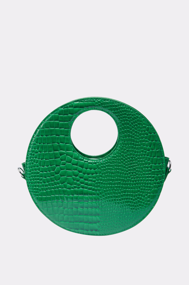 THE CIRCLE PURSE is a round, bright green handbag with a crocodile skin texture and a large circular cutout handle, shown against a light gray background. 1