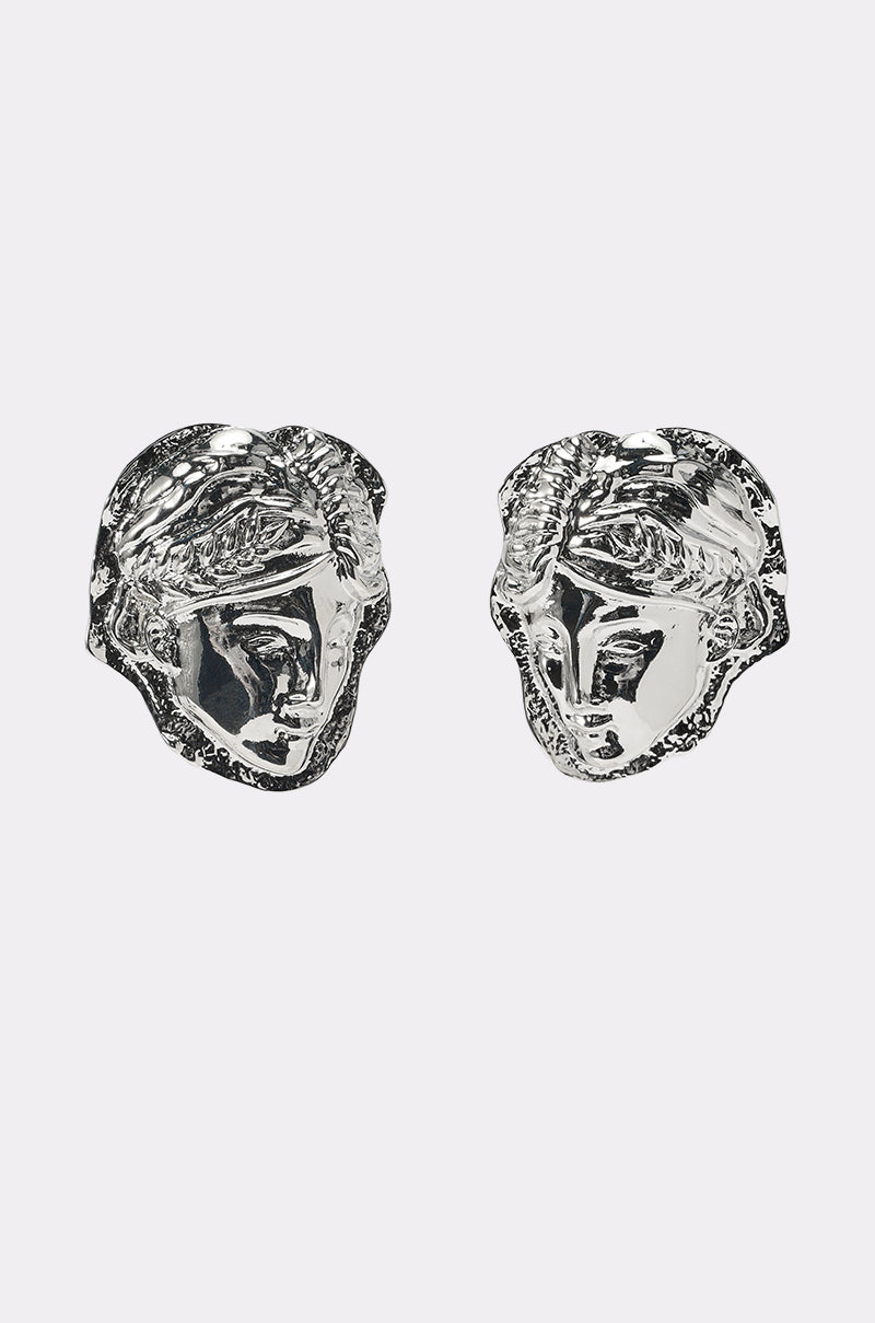 IM IN ITALY EARRING: Silver earrings shaped like stylized classical faces with laurel wreaths, shown against a plain white background. 0