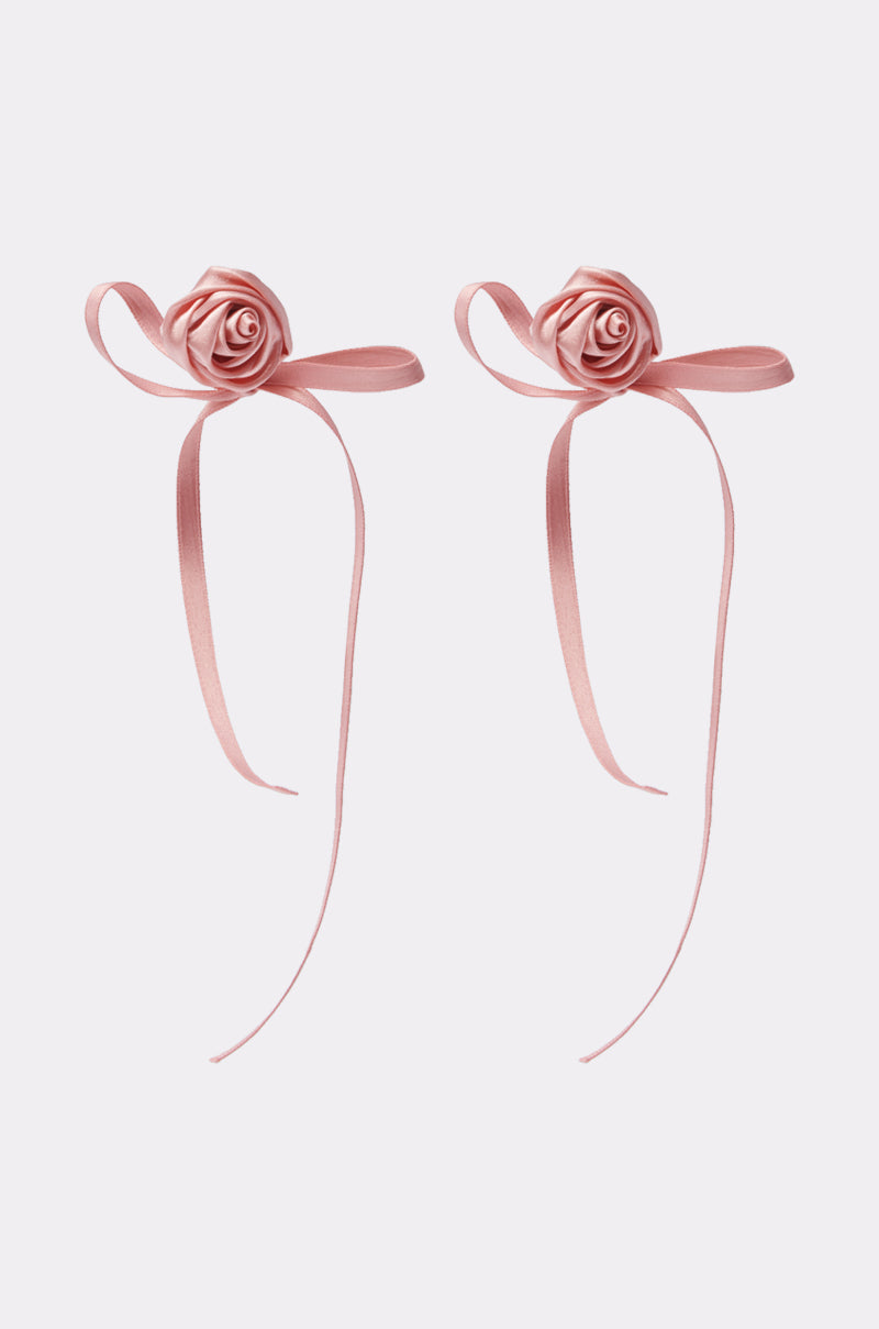 The COQUETTE LOVE EARRING features two pink satin ribbon bows shaped like roses with long trailing ends, displayed side by side on a plain light background. 0