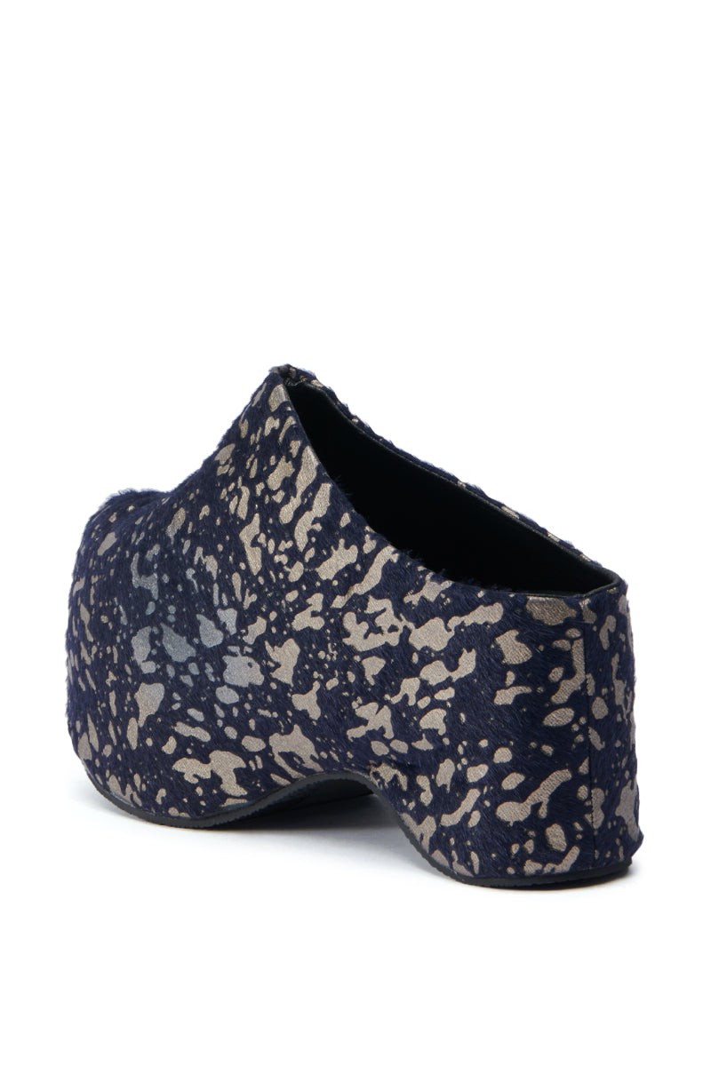 A single AZALEA WANG TEATREE BLACK CLOG in a blue and beige speckled design, showcasing a faux pony hair texture, is seen from the side and slightly behind. This shoe features a chunky, rounded sole with a distinctive abstract pattern.