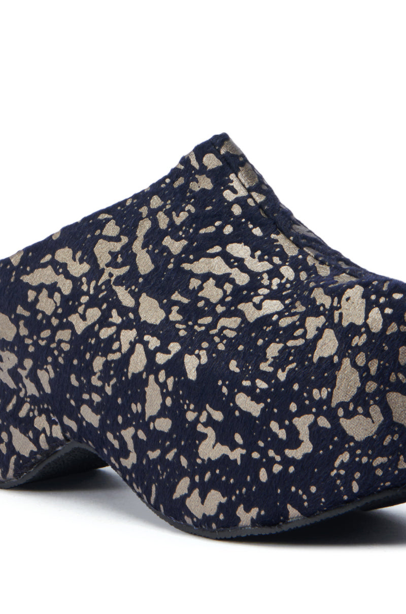 A close-up of the AZALEA WANG TEATREE BLACK CLOG showcases a slip-on design with a dark blue base adorned by a metallic gold speckled pattern. The textured faux pony hair surface pairs with a slightly elevated, chunky heel, creating an elegant yet subtly stylish look.