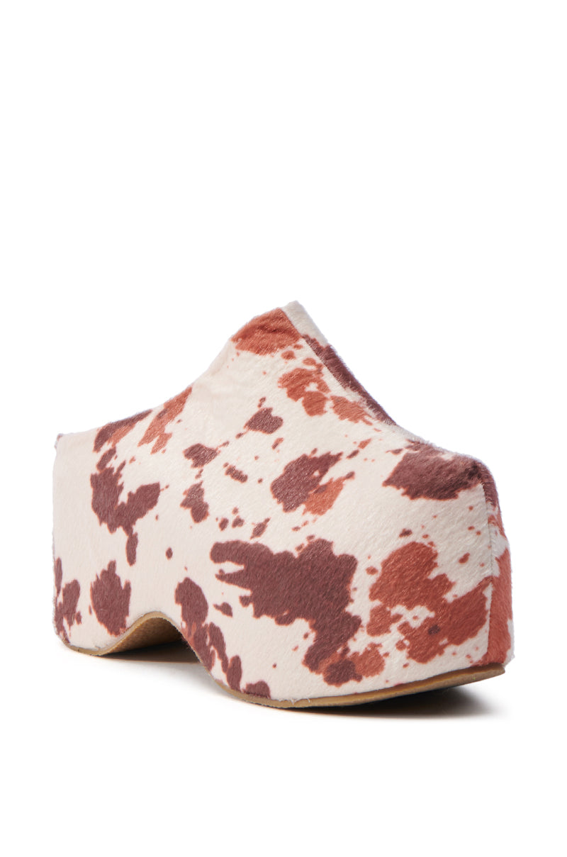 The AZALEA WANG TEATREE COW CLOG features a brown and white cow print in faux pony hair, a chunky platform sole, and a smooth design without visible laces or fastenings, offering all-day comfort with its cushioned insole.