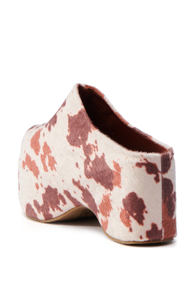 The AZALEA WANG TEATREE COW CLOG showcases a back view with a brown and white cow print design in faux pony hair. This slip-on clog features a chunky wedge and a Comfort Cushion Insole for outstanding wearability.
