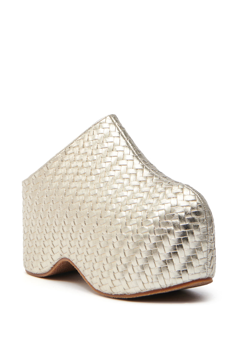 The AZALEA WANG TEATREE GOLD WOVEN CLOG is a silver mule crafted from metallic vegan leather, featuring a high platform sole and closed toe. Displayed at an angle on a white background, its textured rattan-like design adds a modern touch of elegance.