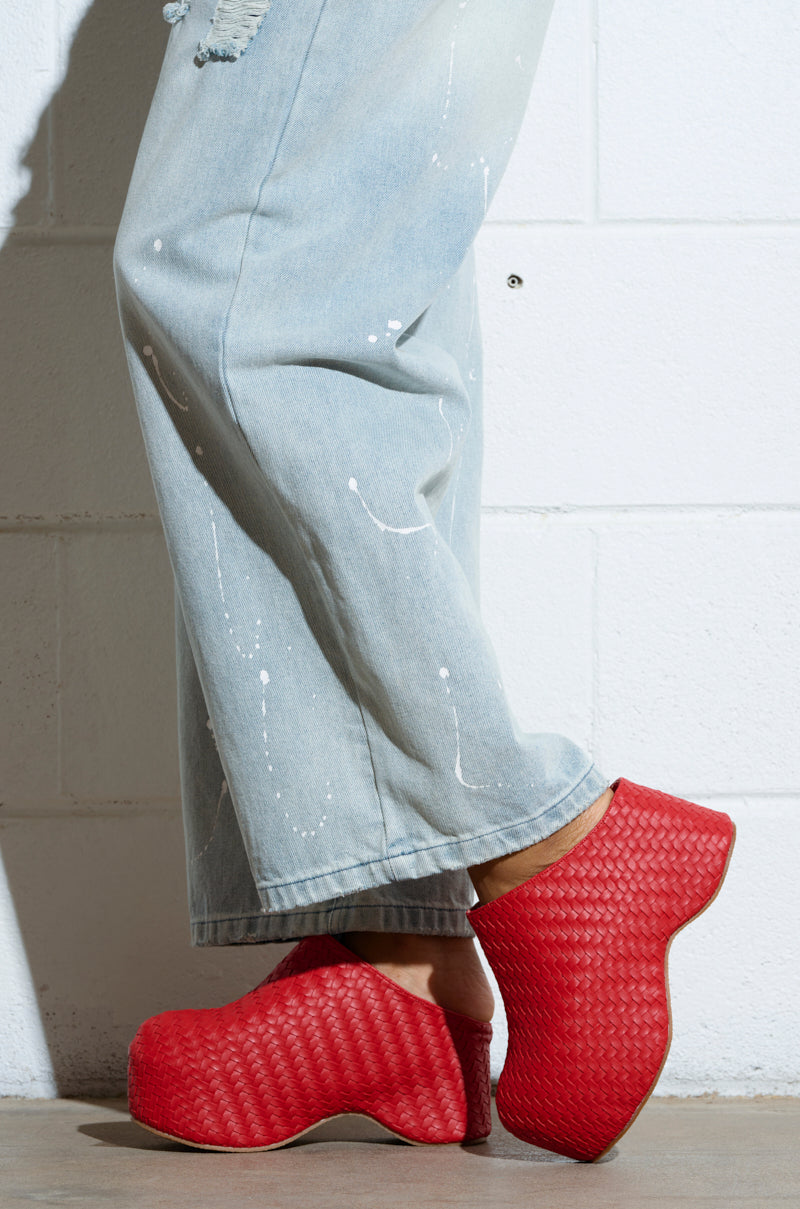 Person in light blue distressed jeans and vibrant red AZALEA WANG TEATREE CLOG platform shoes with a bold chunky heel, standing against a white brick wall.