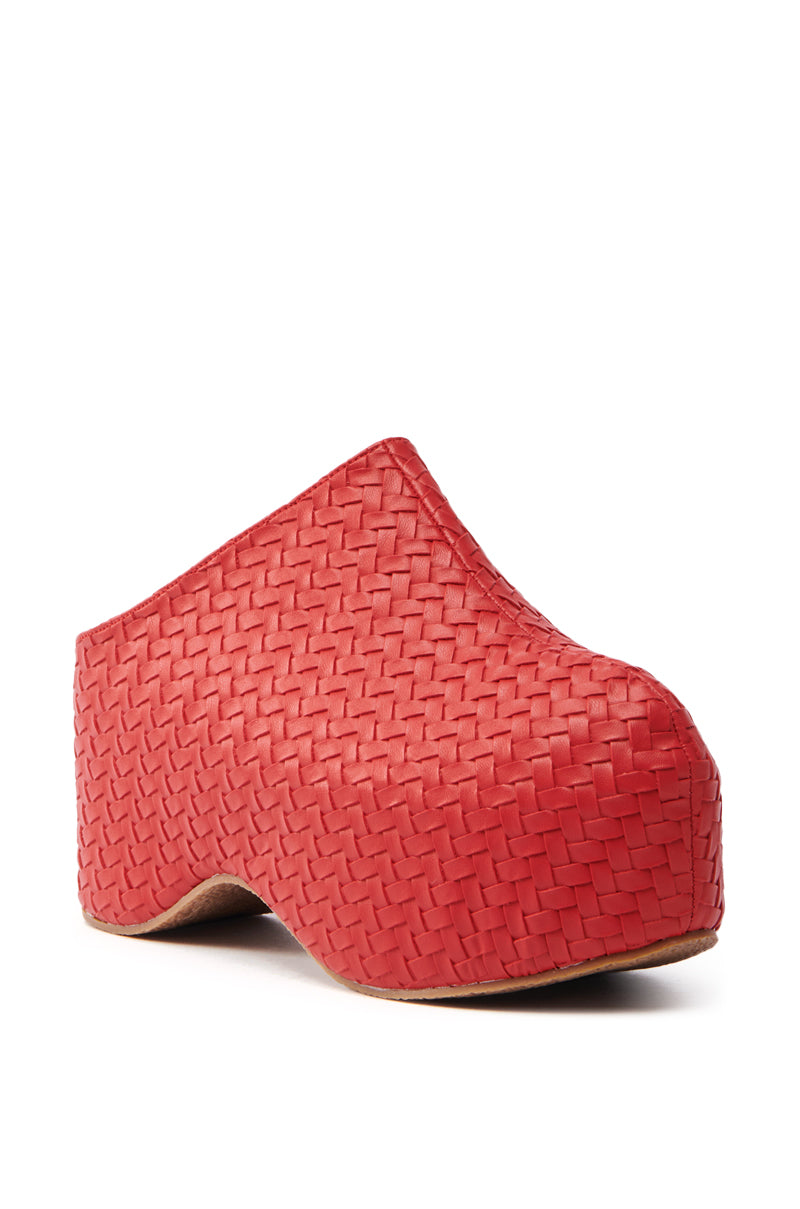 The AZALEA WANG TEATREE RED CLOG is a stylish red clog with a woven texture, featuring a thick flatform sole and closed toe. Crafted from vegan leather, it showcases a unique design angled slightly to the left.