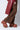 A person dressed in brown leopard-print pants and a red leather coat is standing on tiptoe. They are wearing the AZALEA WANG TEATREE RED SNAKE FLATFORM CLOGS, which feature a colorful snake-skin pattern and a flatform sole, offering both style and support. The background is plain white.