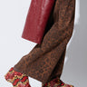 A person dressed in brown leopard-print pants and a red leather coat is standing on tiptoe. They are wearing the AZALEA WANG TEATREE RED SNAKE FLATFORM CLOGS, which feature a colorful snake-skin pattern and a flatform sole, offering both style and support. The background is plain white.