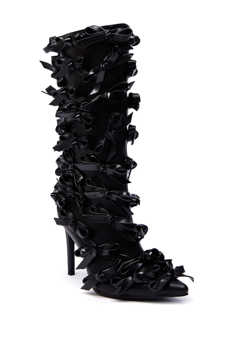 The AZALEA WANG TELMO BLACK BOW EMBELLISHED BOOTIE is a knee-high stiletto bootie made from luxe faux leather, featuring multiple decorative black ribbon bows for a bold and textured fashion statement.