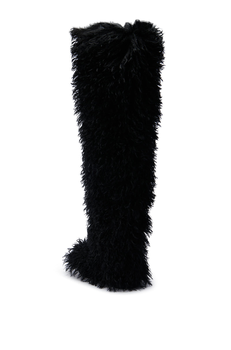 The AZALEA WANG TEMPLETON BLACK POODLE FUR OVER THE KNEE BOOT is a knee-high, plush black boot with a textured faux-fur design reminiscent of poodle fur. It features a pointed toe and stands upright against a white background.