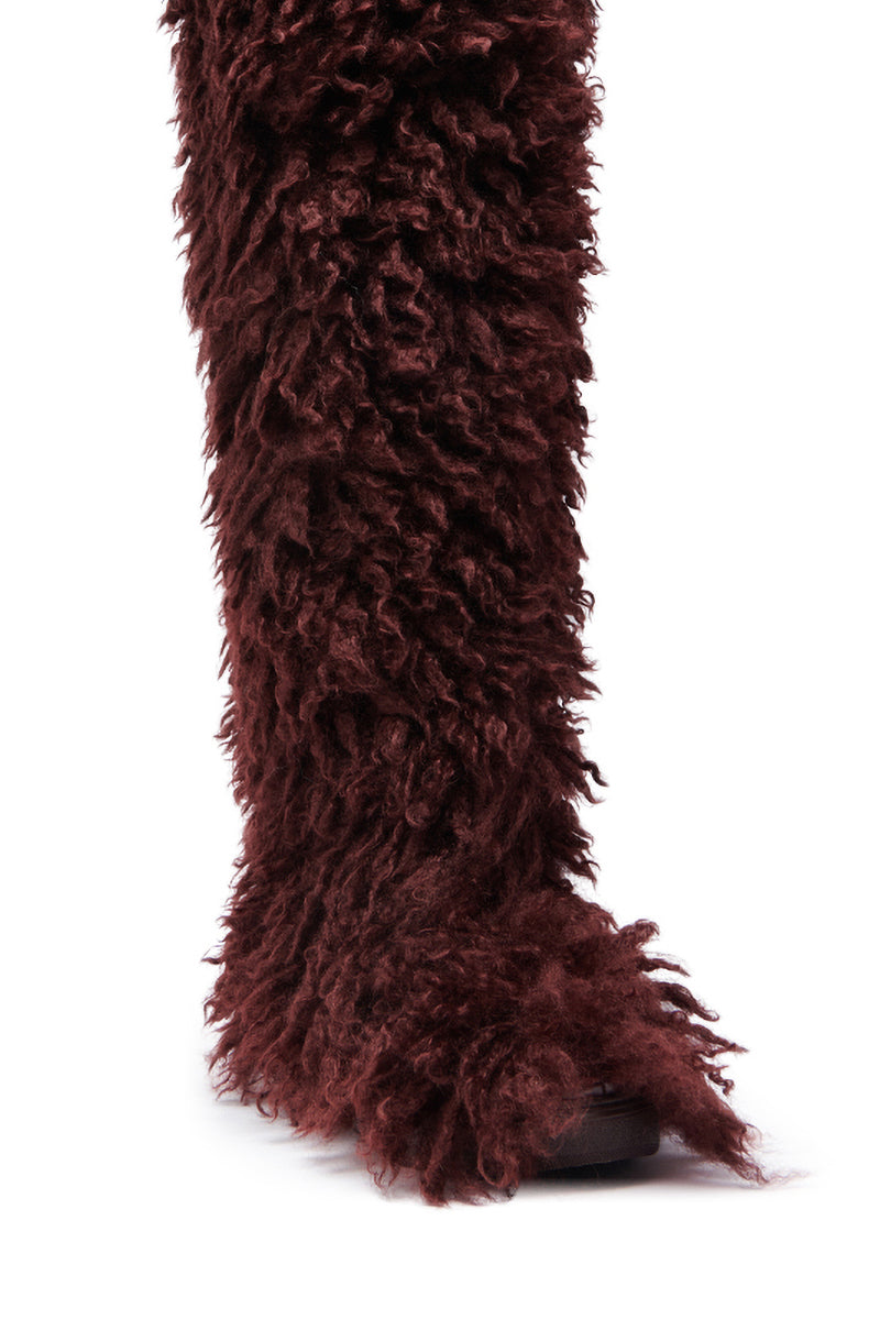 A close-up of the AZALEA WANG TEMPLETON BURGUNDY POODLE FUR OVER THE KNEE BOOT, featuring thick, curly dark burgundy fur that covers the shape and extends all the way to the floor.