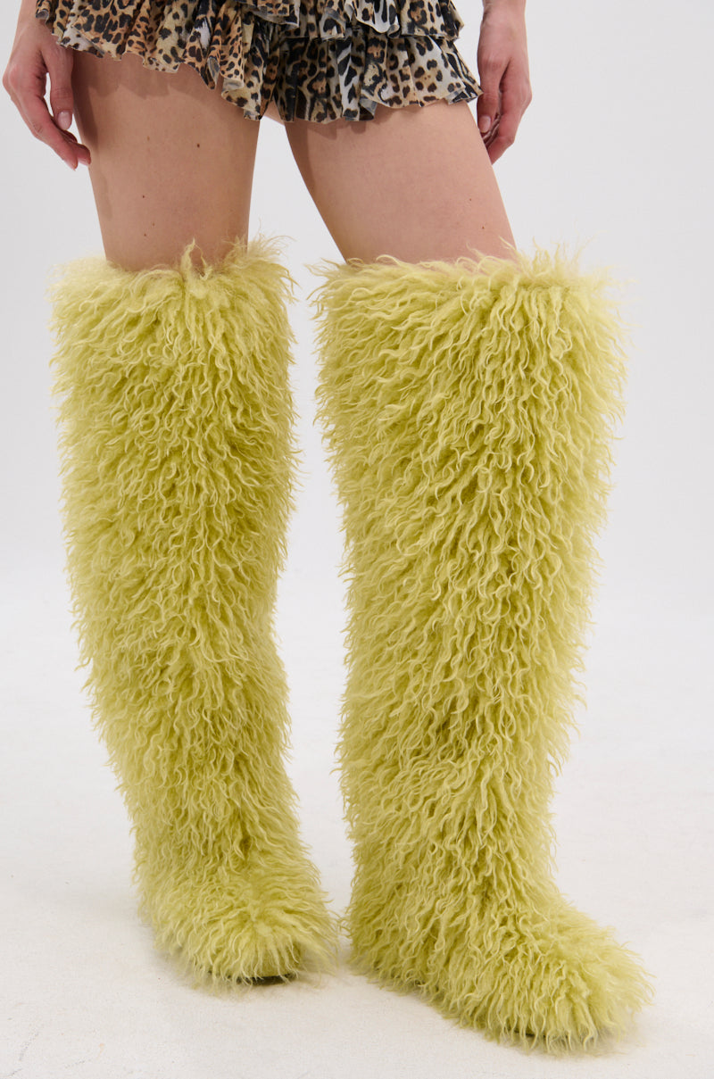 A person wears the AZALEA WANG TEMPLETON LIME POODLE FUR OVER THE KNEE BOOT with a short, ruffled brown and black leopard print skirt against a plain white background.