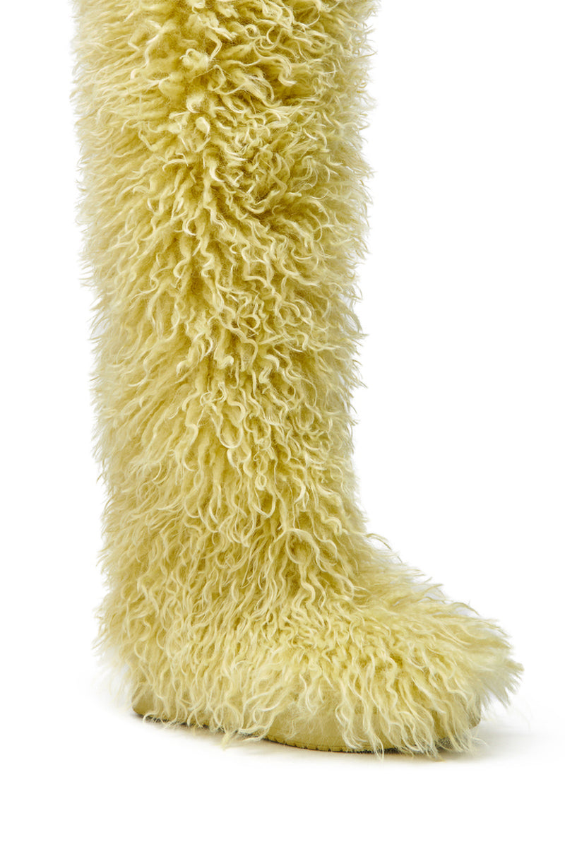 A close-up of AZALEA WANG TEMPLETON LIME POODLE FUR OVER THE KNEE BOOT, featuring shaggy yellowish faux fur resembling a fluffy animal’s leg, displayed against a white background.