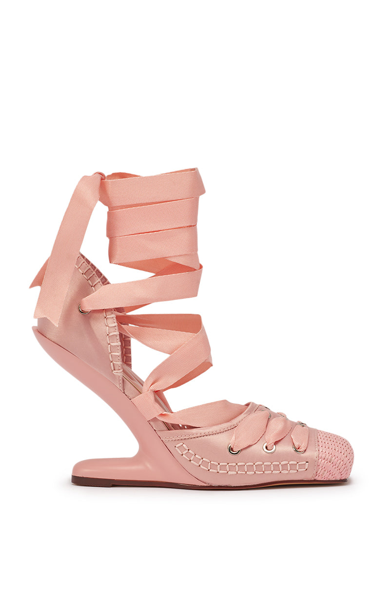 The AKIRA GOLD TENDU PINK BALLET LACE UP NOVELTY HEEL PUMP is a stylish pink sandal with a unique curved wedge heel, woven toe detail, and satin ribbon laces that wrap around the ankle and lower leg. 3