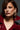 A woman with wavy brown hair wears a glossy dark red coat and the vibrant DONATELLA EARRING, featuring teardrop pearl accents. She gazes to the side against a dark gray background.