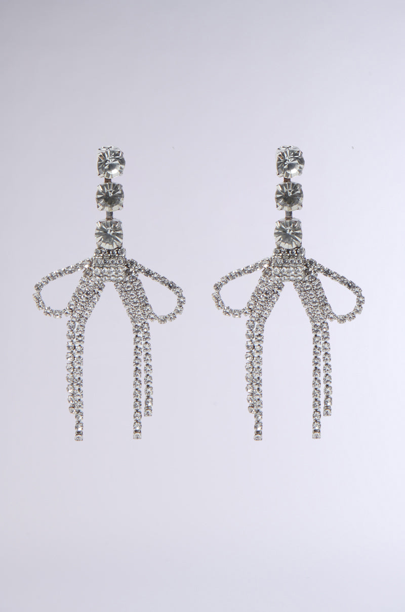 WITH A BOW SILVER EARRING: Elegant silver rhinestone fringe earrings shaped like bows, each featuring cascading sparkling strands against a light gray background.