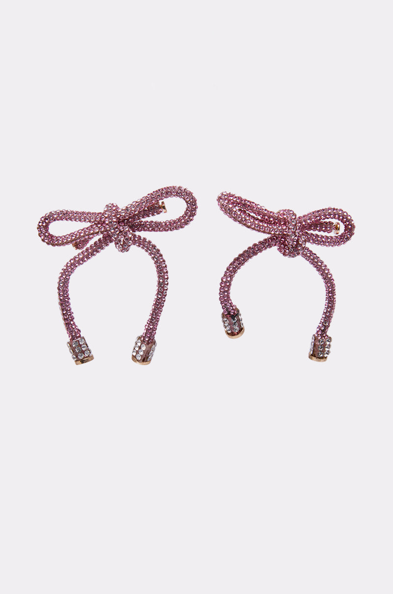 The ALL NIGHT LONG LIGHT PINK EARRING features a pair of sparkling pink rhinestone bow earrings with dangling ends, each tip embellished with silver-tone rhinestone accents, shown against a plain white background. 4