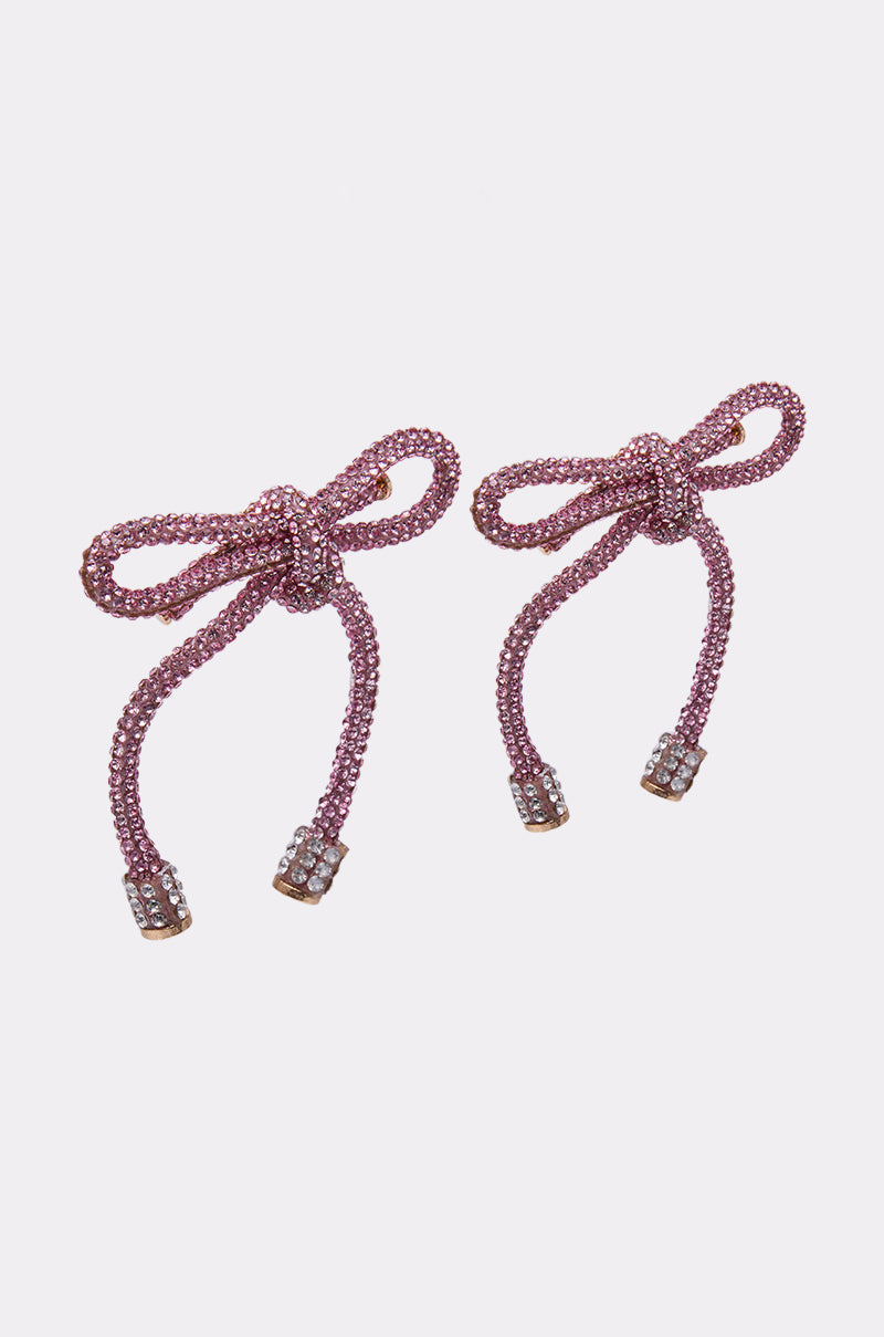 The ALL NIGHT LONG LIGHT PINK EARRING features delicate bow shapes with rhinestone clusters at the ends, all shown against a plain white background. 5