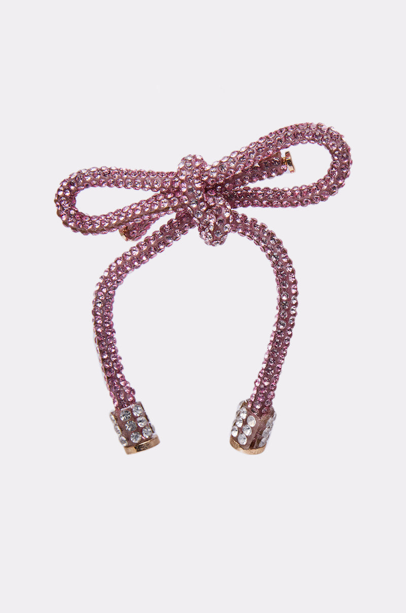 The ALL NIGHT LONG LIGHT PINK EARRING features a sparkling bow design covered in pink rhinestones, with two dangling ends capped in clusters of clear crystals, displayed on a plain white background. 6