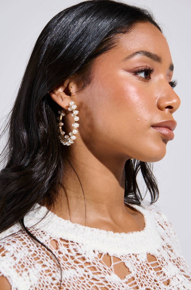 A woman with long black hair showcases the EVERYTHING YOU WANT EARRING, featuring large hoops with delicate pearl detailing. She wears a textured white top as her profile is captured against a plain background, accentuating her radiant skin. 4