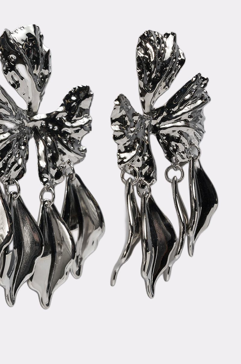 The IN BLOOM EARRING features shiny, abstract silver-tone dangle elements with textured, organic shapes like leaves or petals—unique statement earrings shown on a plain white background. 6