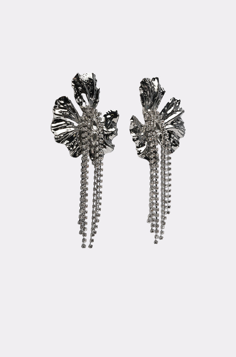 The ON A TRIP EARRING features metallic silver-tone drop earrings shaped like abstract flowers with textured petals and dangling chains, displayed on a plain white background. 2