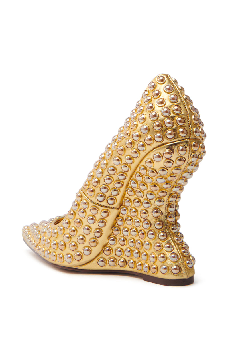 The AZALEA WANG TERYN GOLD WEDGE PUMP features a sculptural high-heel with a unique curved design, crafted in metallic vegan leather and embellished with silver studs for a textured, modern aesthetic showcasing intricate detailing and craftsmanship.