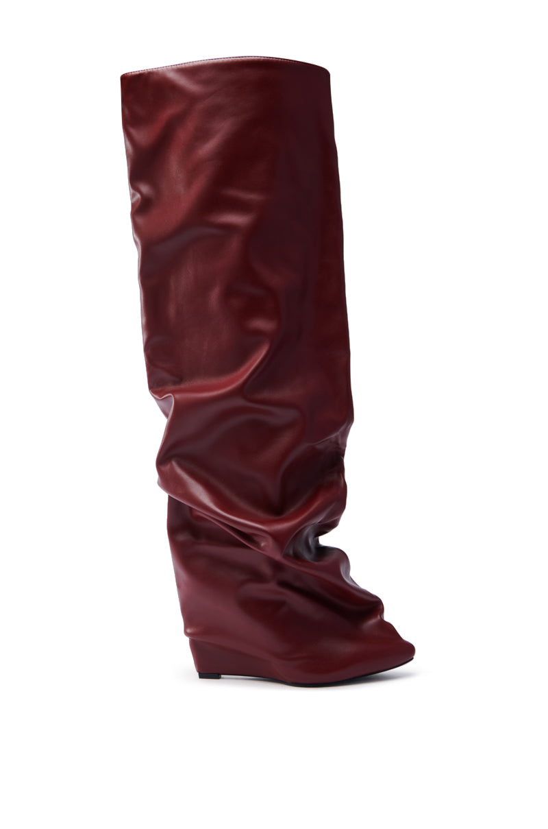 The AZALEA WANG TEUILA BURGUNDY WEDGE RUCHED BOOT stands elegantly against a white background, featuring a tall, slouchy design made of shiny burgundy faux leather with a slightly pointed toe and low wedge heel.