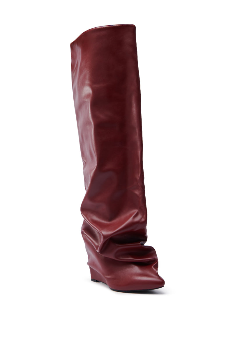 The AZALEA WANG TEUILA BURGUNDY WEDGE RUCHED BOOT, a single tall faux leather boot with a slouchy design and hidden wedge heel, stands upright against a plain white background, exuding the sophisticated allure of thigh-high boots.