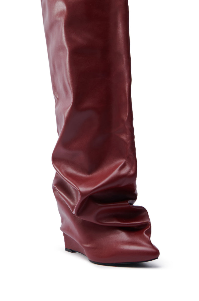 The AZALEA WANG TEUILA BURGUNDY WEDGE RUCHED BOOT features a close-up of a burgundy wedge with a slightly pointed toe, low heel, and soft faux leather gathered at the ankle for a fashionable look.