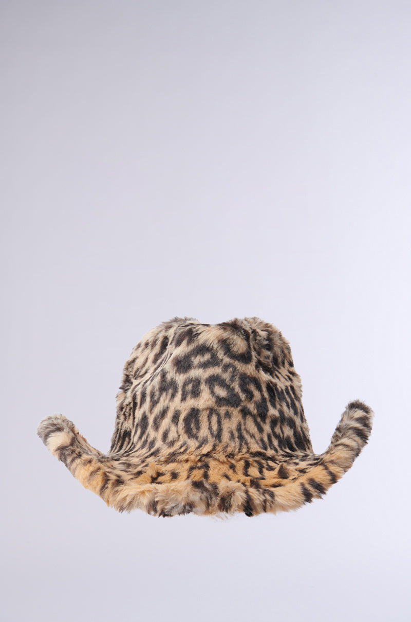 The "CHECK ME OUT FAUX FUR COWBOY HAT," with its leopard print design and wide, slightly flared brim reminiscent of a Western accessory, is displayed against a plain gray background. The hat showcases a pattern featuring spots in shades of brown and black.