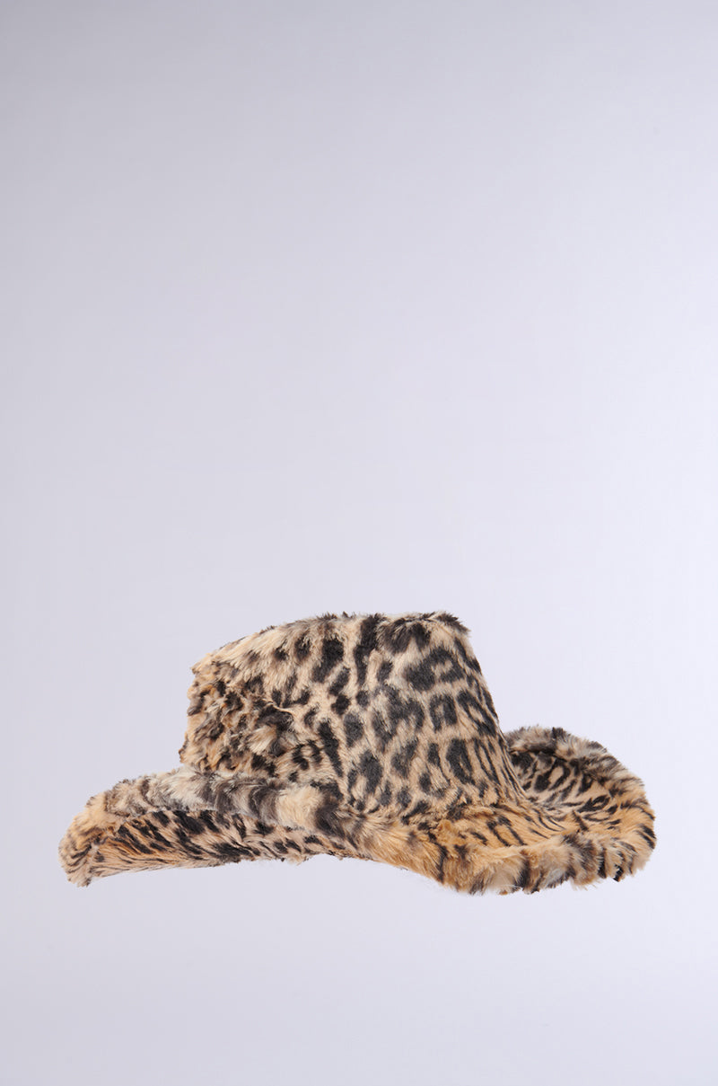 The CHECK ME OUT FAUX FUR COWBOY HAT, featuring a striking leopard print, makes a bold statement against a plain gray background. Its expansive brim and soft, textured look bring together daring fashion elements with timeless Western allure.