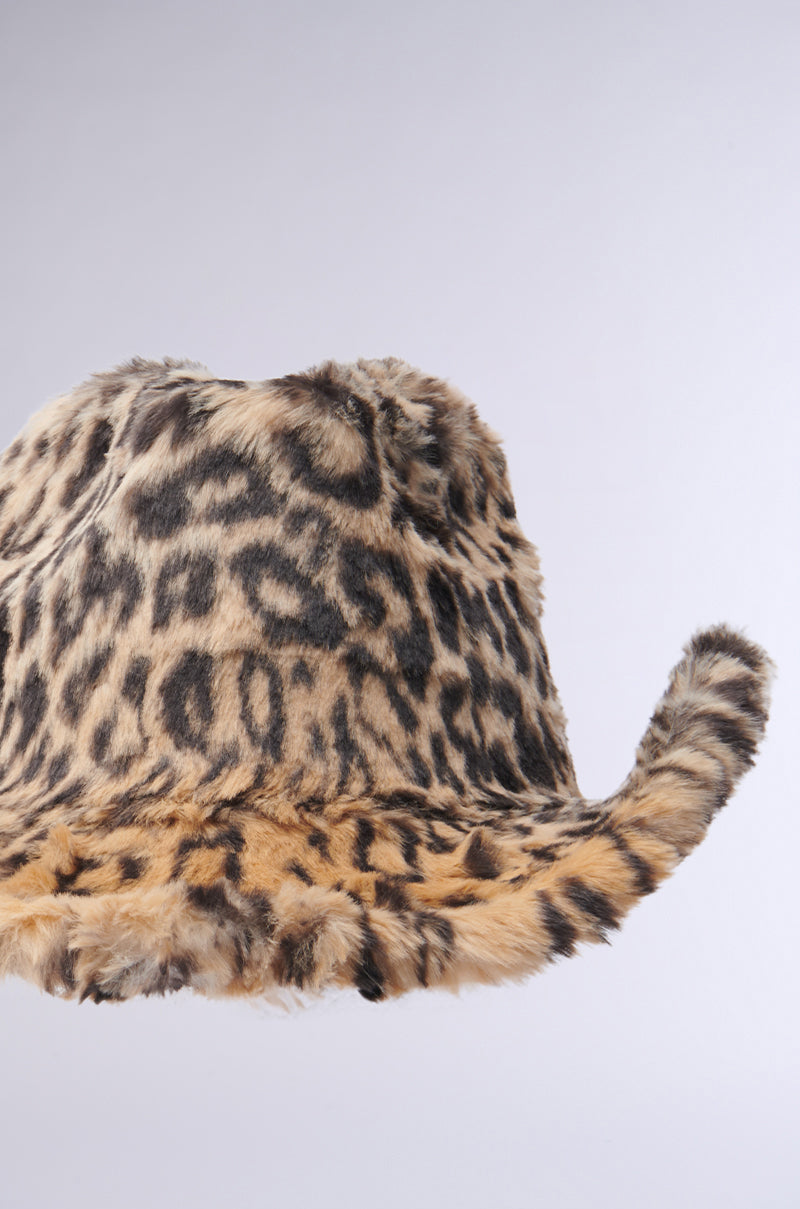 The CHECK ME OUT FAUX FUR COWBOY HAT is displayed against a plain background, featuring a wide, slightly curled brim adorned with an array of tan, brown, and black spots. This pattern authentically resembles a leopard's distinctive appearance—transforming it into a striking Western accessory. 9