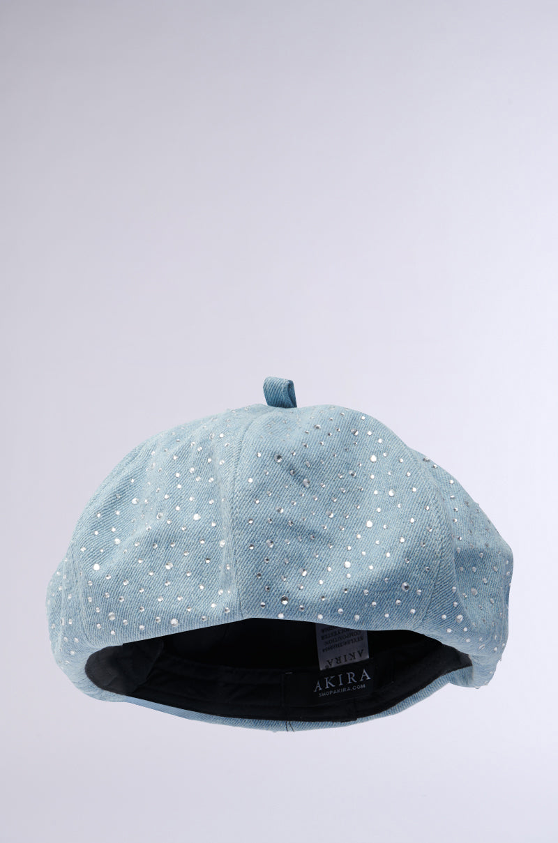 The SEE ME COMING BLING BERET is a light blue accessory embellished with shiny rhinestones. It features a dark interior with a visible tag, set against a soft gradient background transitioning from light gray to white for a clean, minimalistic look.