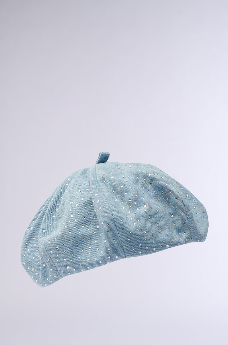 The SEE ME COMING BLING BERET, in light blue with small white polka dots, adds playfulness. Subtle rhinestones enhance its charm, featuring a top loop and displayed against a plain gradient backdrop.