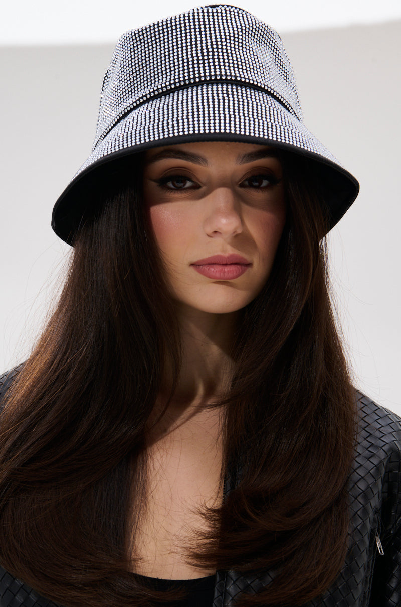 A woman with long, dark hair wears the PAY ME BLING BUCKET HAT and a black textured jacket, looking directly at the camera with a neutral expression against a plain background.