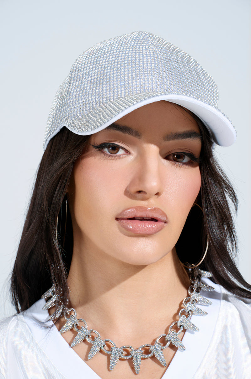 A woman with long dark hair wears the IM RICH BLING SNAPBACK with a rhinestone overlay and adjustable strap, paired with large hoop earrings and a chunky silver necklace, looking directly at the camera against a plain background.