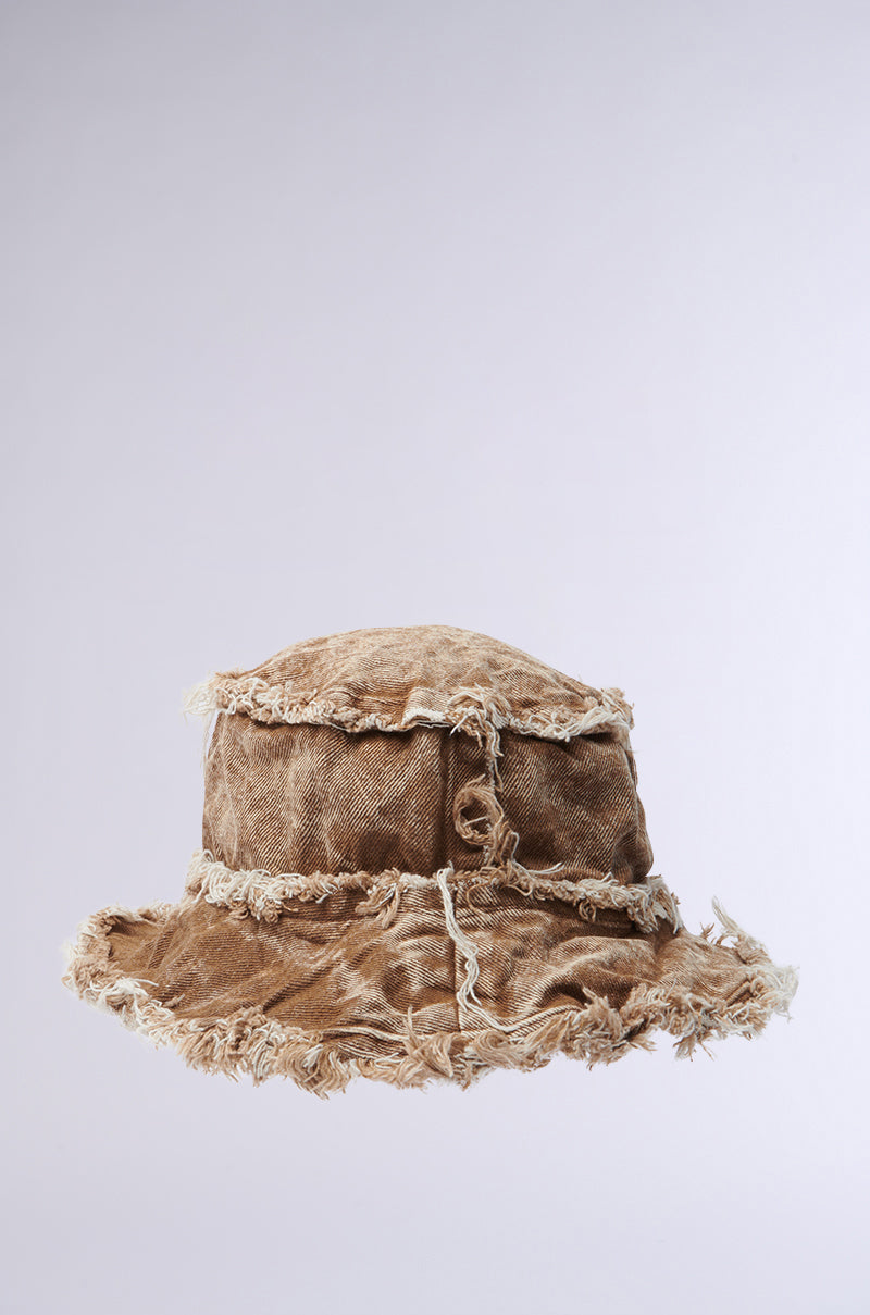 The WITH IT DISTRESSED BUCKET HAT features a brown, vintage-washed fabric with frayed edges and visible stitching, showcased against a plain light gray background.