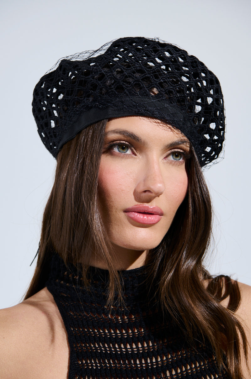 A person with long brown hair dons a TOO EDITORIAL CUTOUT BERET and a matching halterneck top, gazing slightly to the side against a plain backdrop. Green eyes and pink lips are highlighted by natural makeup, while their expression remains neutral.