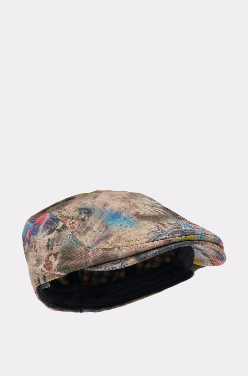 The IM OUTSIDE GRAFFITI HAT is a newsboy-style cap with a multicolored abstract pattern in brown, blue, red, and yellow. It features an adjustable headband and is shown against a plain white background. 3