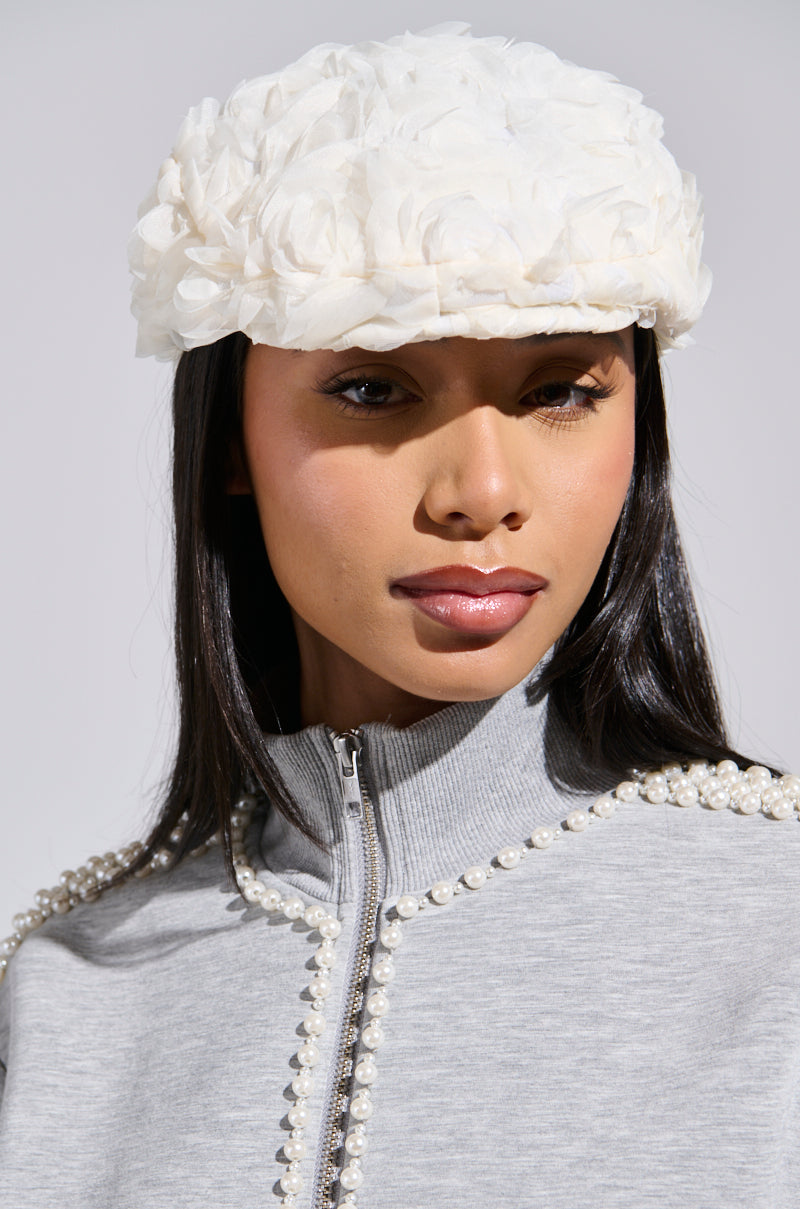 A person wearing a light gray jacket with pearl details and a SO DEMURE ROSETTE HAT. The neutral background perfectly highlights the outfit and accessories.