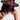 A woman in the ALIYA FLORAL BRIM HAT, with floral appliqués, gazes down. Her long dark hair flows over a white crop top, adorned with a pearl necklace and a red leather strap with metal studs. The scene unfolds against a plain gray backdrop, exuding AKIRA Label charm.