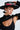 A person, wearing an ALIYA FLORAL BRIM HAT and black outfit, poses with closed eyes, featuring a septum piercing and white rectangular earrings. With one arm raised, a snake tattoo on their chest is elegantly revealed.