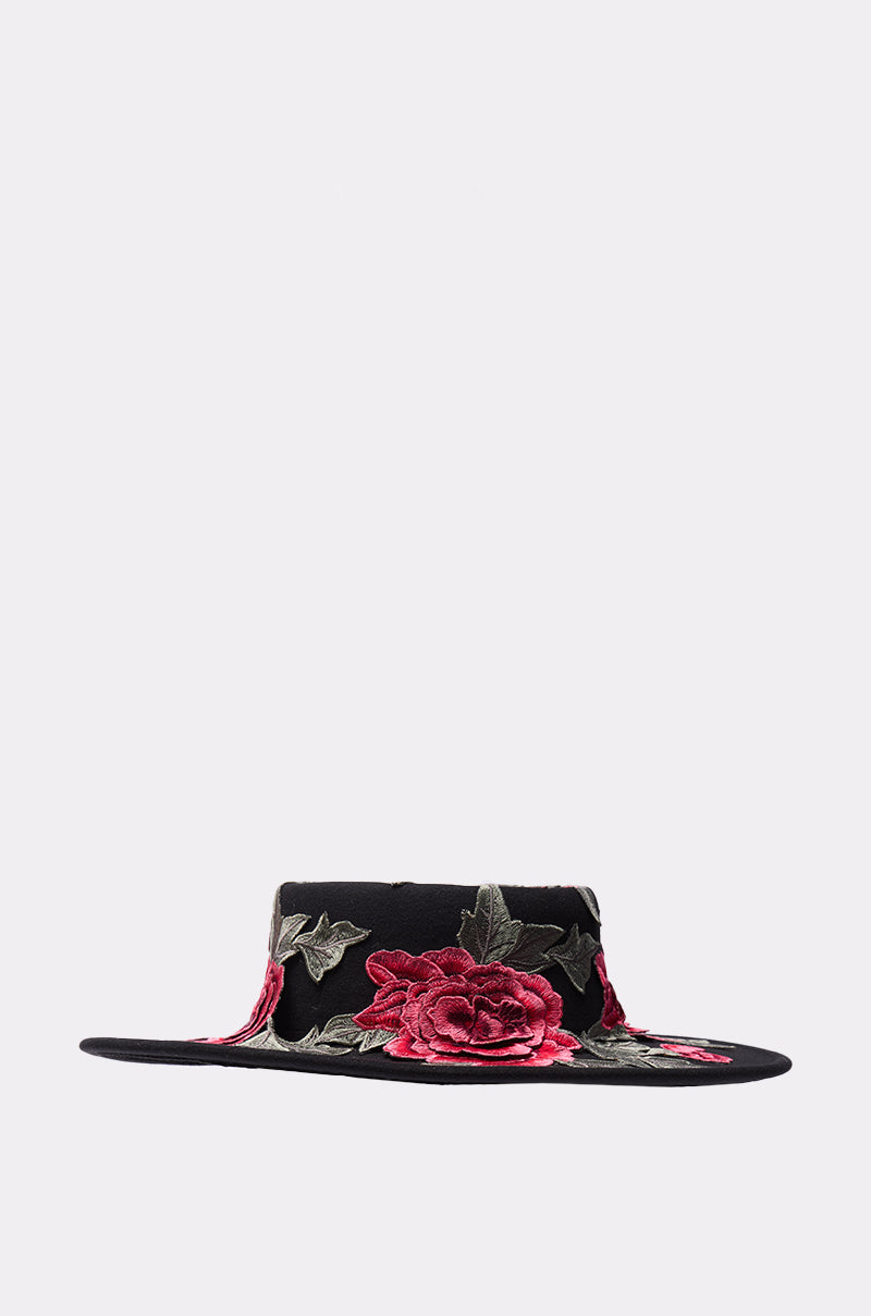 The ALIYA FLORAL BRIM HAT is a black wide brim hat featuring embroidered red and pink roses with green leaves along the brim and crown, shown against a plain light gray background. 2