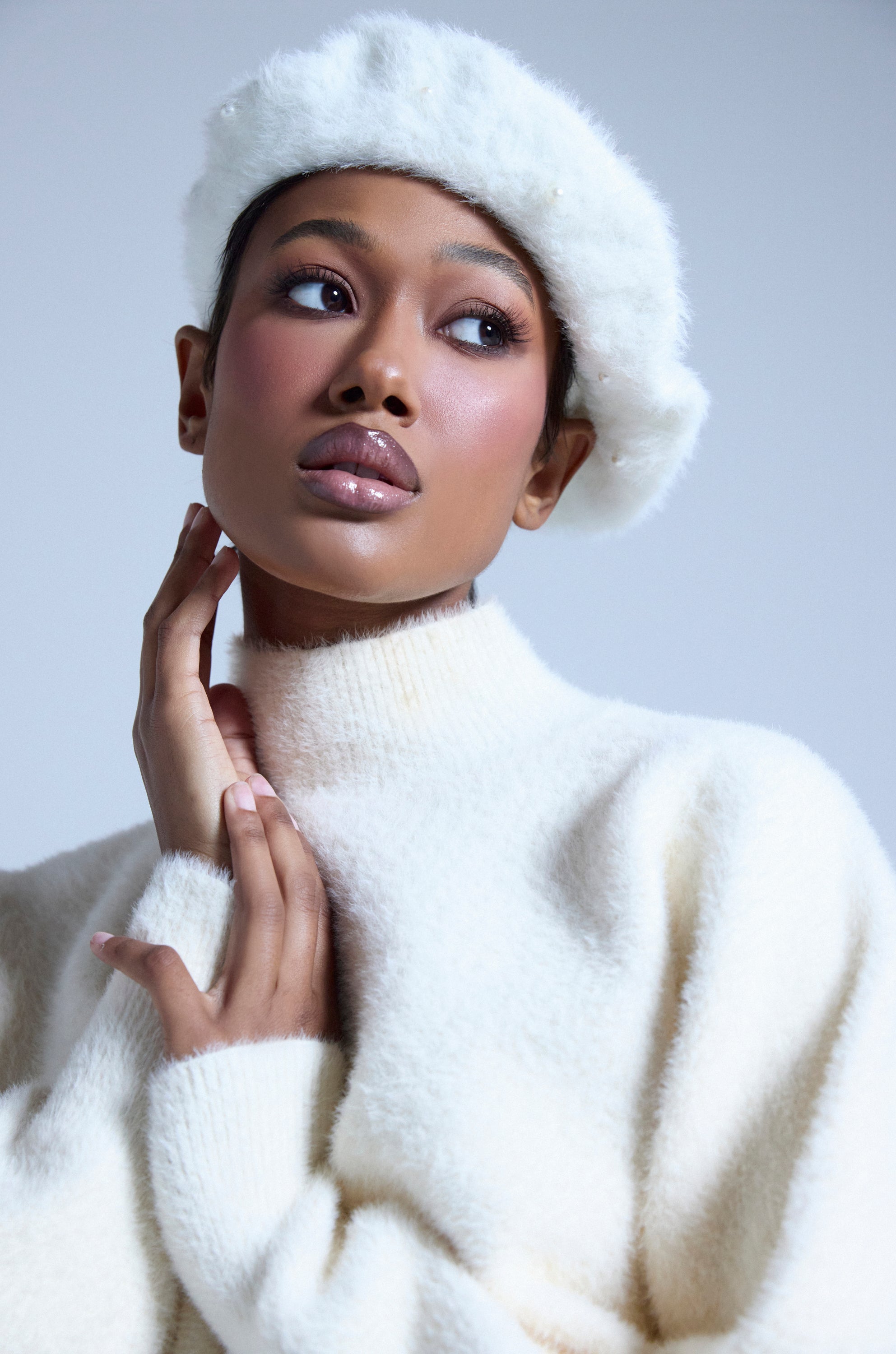 Wearing the PEARLY WHITES FLUFFY BERET and a matching white turtleneck, a woman poses with one hand to her neck against a light gray background that highlights the mohair-inspired knit of her cozy look. 0
