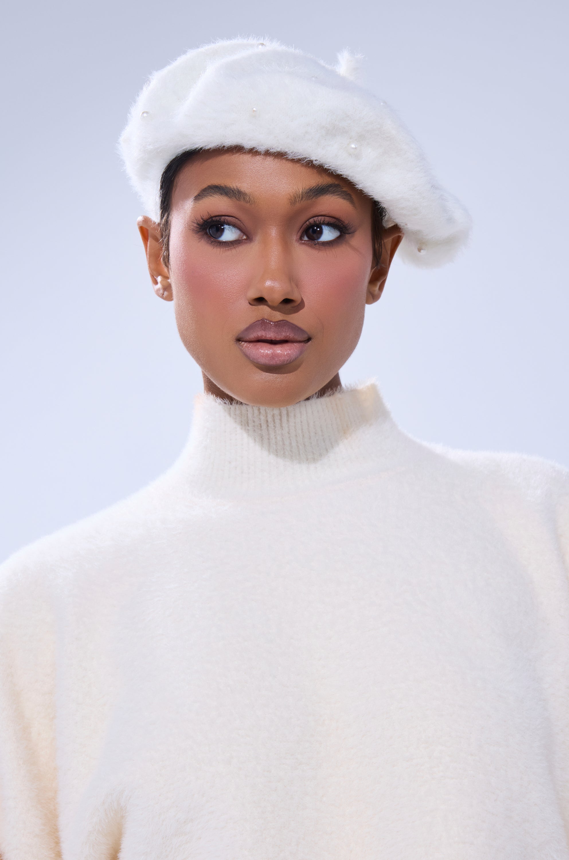A woman wearing the PEARLY WHITES FLUFFY BERET, featuring pearl embellishments, and a high-neck, mohair-style knit sweater looks to the side against a light background. 3