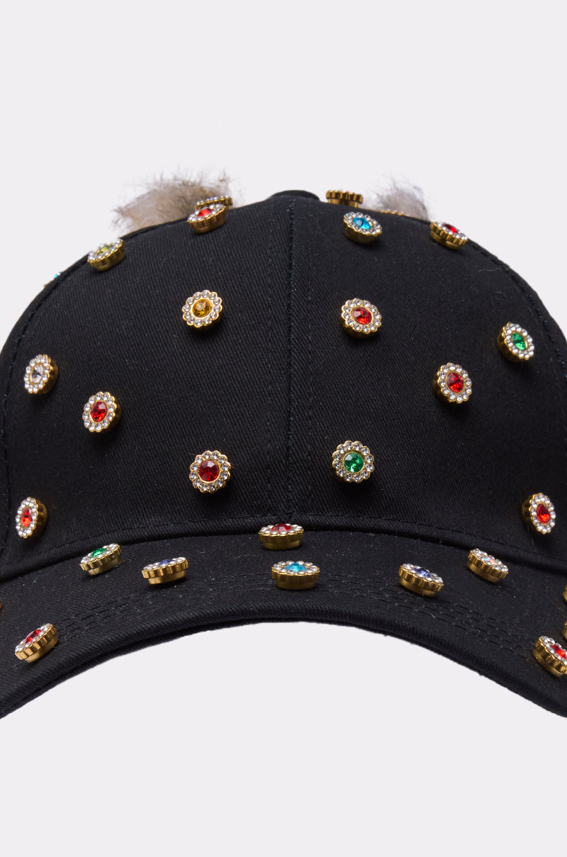 The TJ FAUX FUR EMBELLISHED HAT is a black baseball cap with gold jeweled studs and red, green, and blue stones evenly spaced across the front and brim. 6